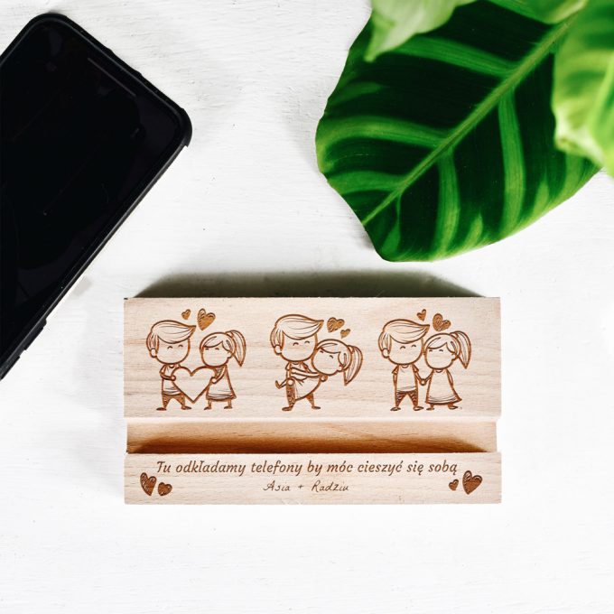 Drewniany stojak na telefon z wygrawerowanym tekstem: Tu odkładamy telefony by móc cieszyć się sobą Asia + Radziu